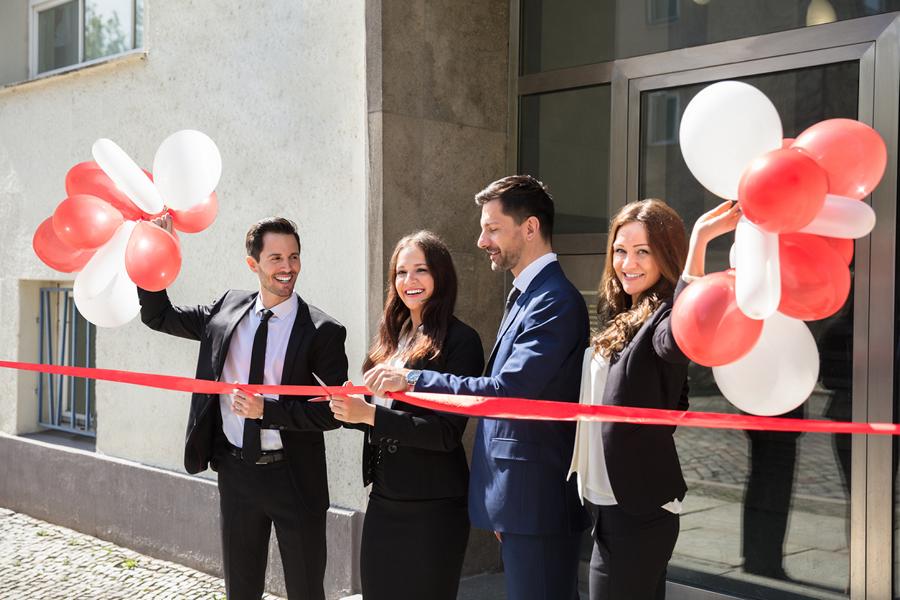 Personen in Businesskleidung durchschneiden rotes Band bei einer Firmenfeier